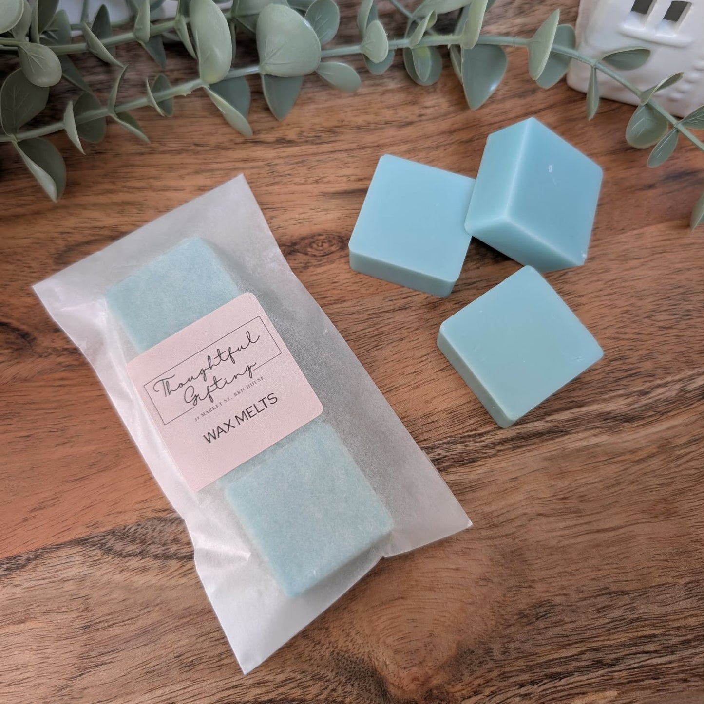 Teal Fresh Linen wax melts with a Personalised Sticker in a glassine envelope on a wooden surface with eucalyptus leaves.