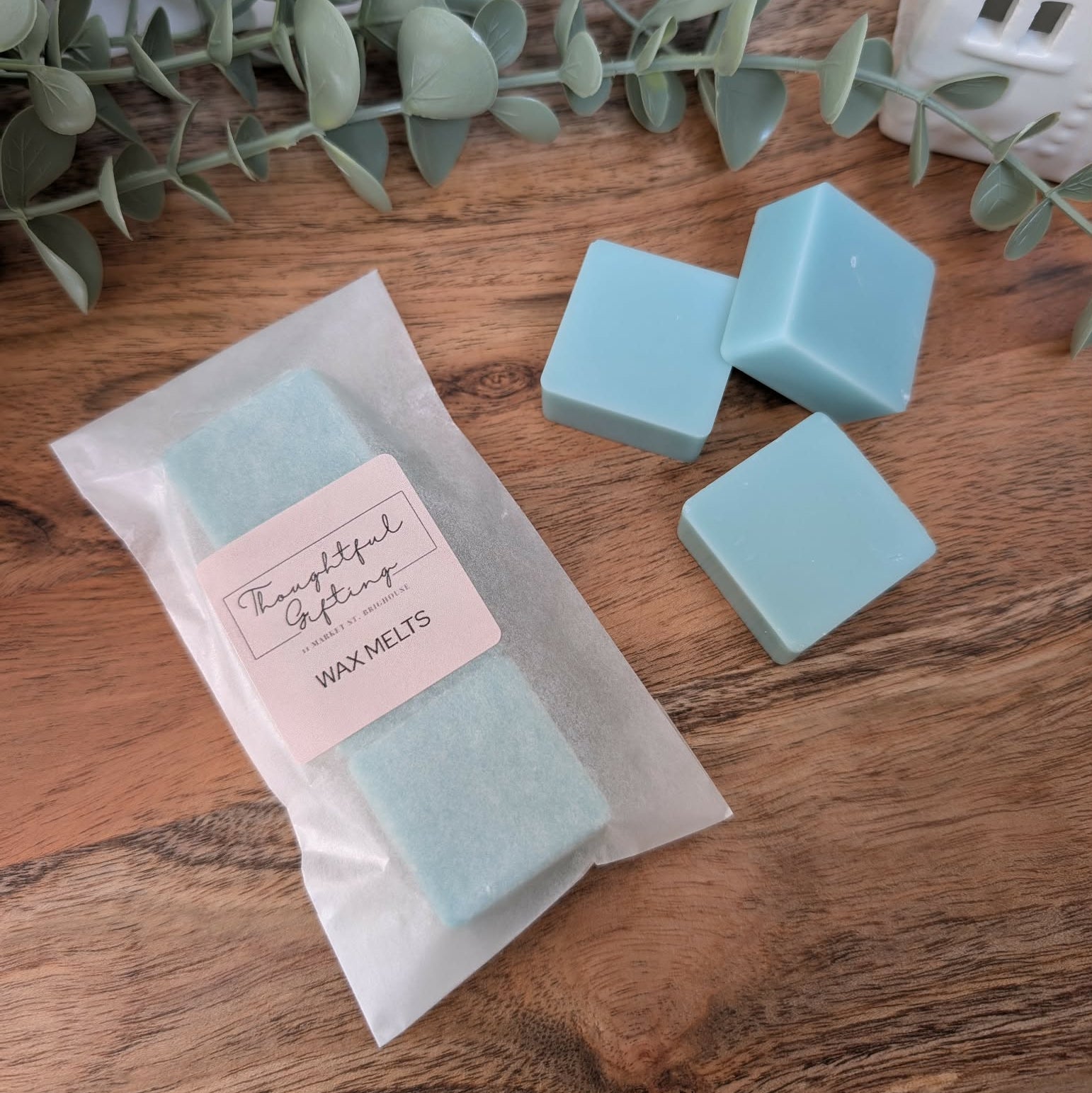 Teal Fresh Linen wax melts with a Personalised Sticker in a glassine envelope on a wooden surface with eucalyptus leaves.