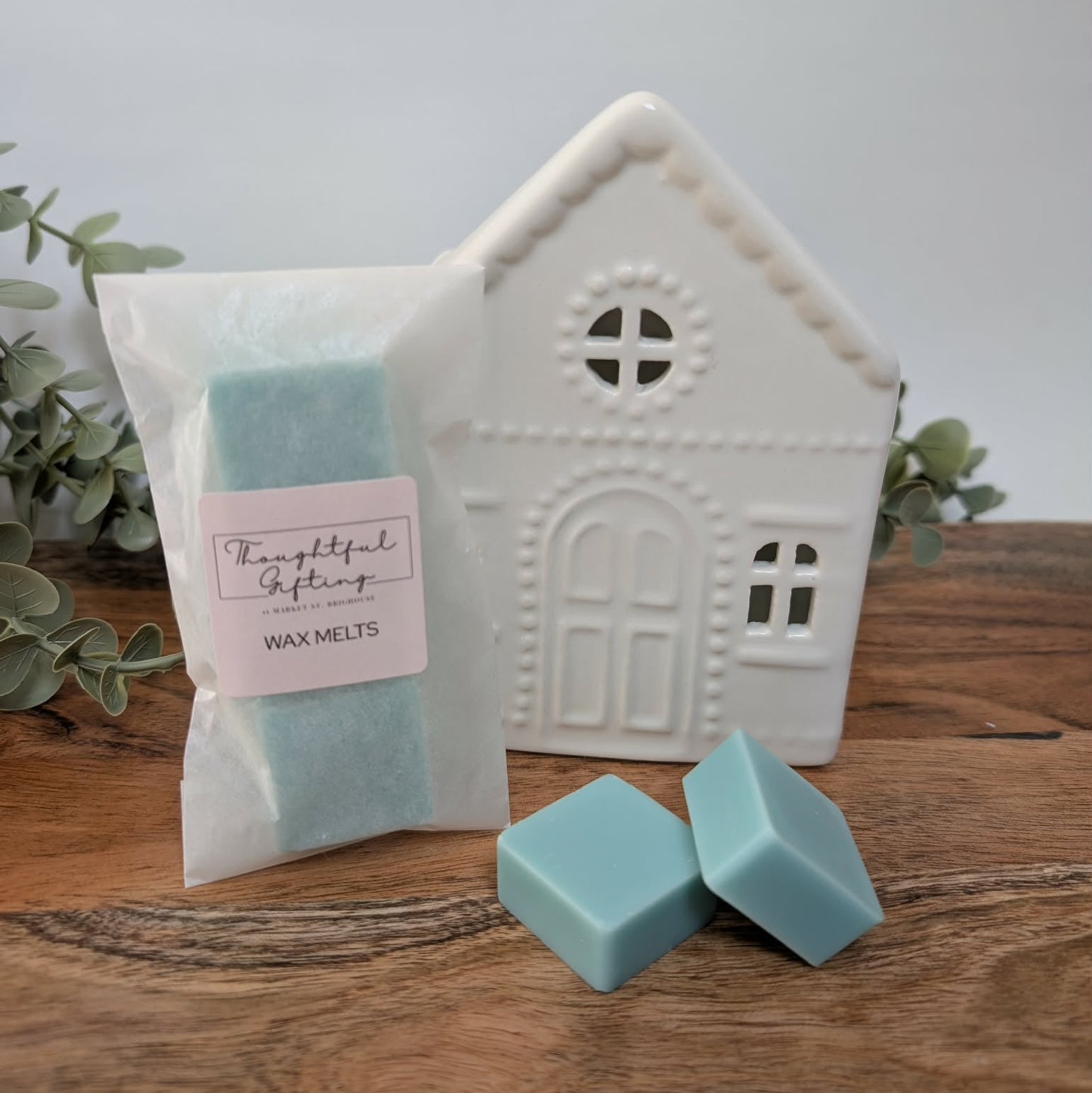 Wax melts packaging with a creamic house-shaped oil burner on a wooden surface.