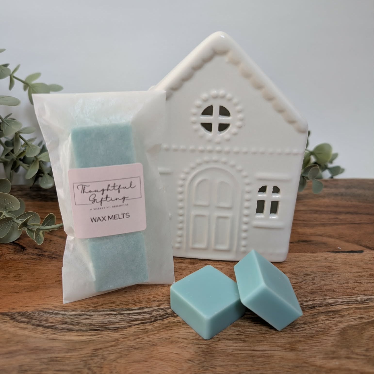 Wax melts packaging with a creamic house-shaped oil burner on a wooden surface.