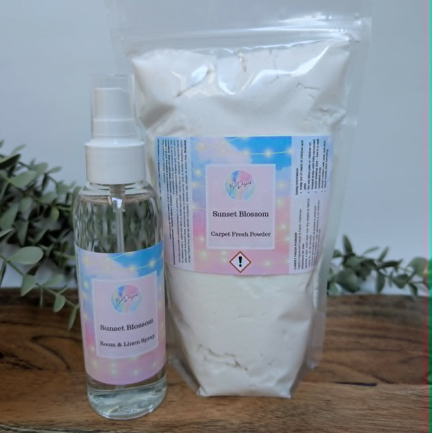 Room Spray PET Bottle and bag of Mrs Hinch Sunset Blossom carpet freshener on a wooden surface with plants in the background.