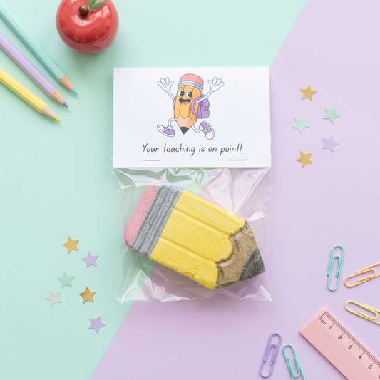 A pencil shaped bath bomb with a pastel green and lilac background surrounded by stationary. The perfect gift for teachers and teaching assistants. End of school term present idea.